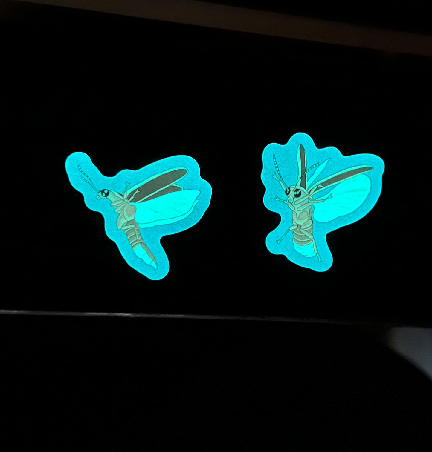 two glow in the dark firefly stickers glowing brightly in full darkness